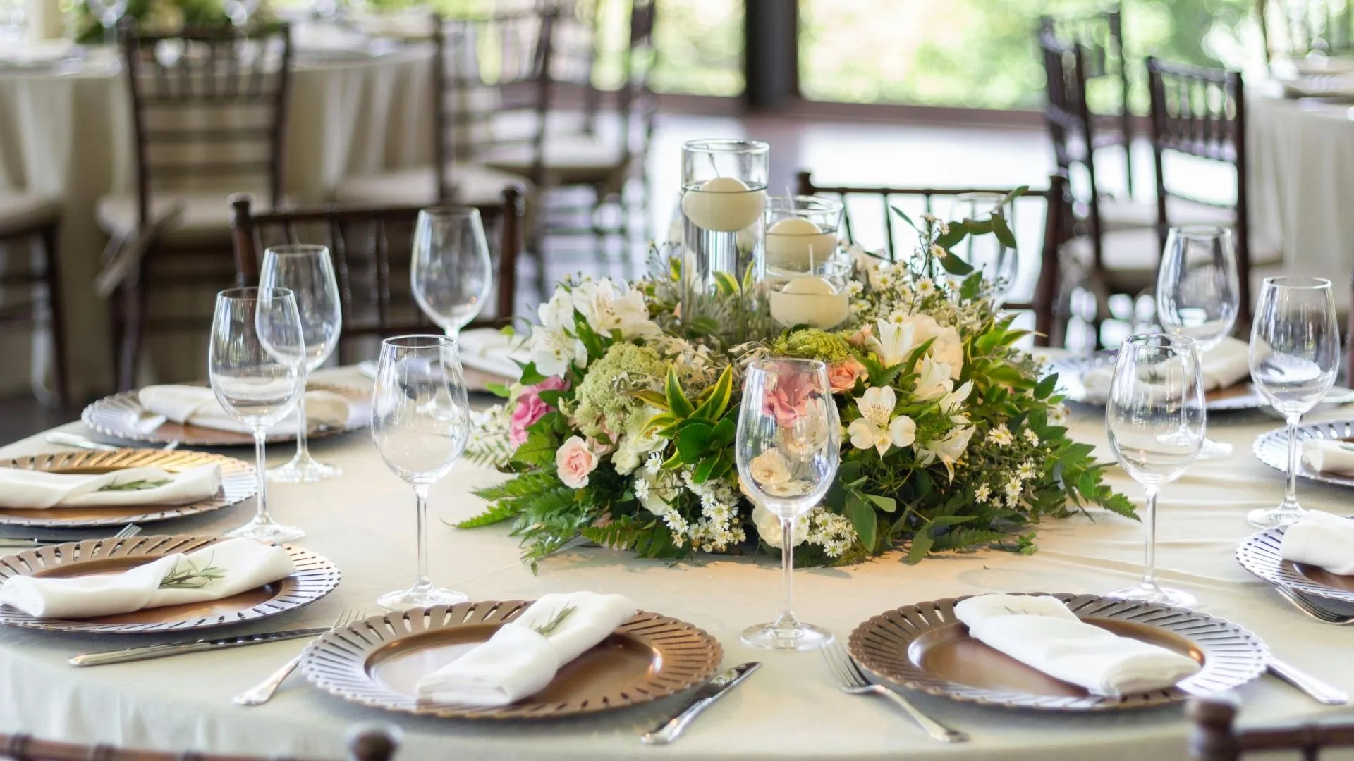 Table ronde de mariage dressée en salle, verrerie, assiettes de présentation et centre de table fleuri